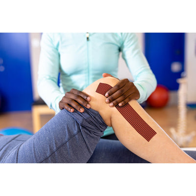 Clinician applying RockTape RHEON kinesiology tape to a knee
